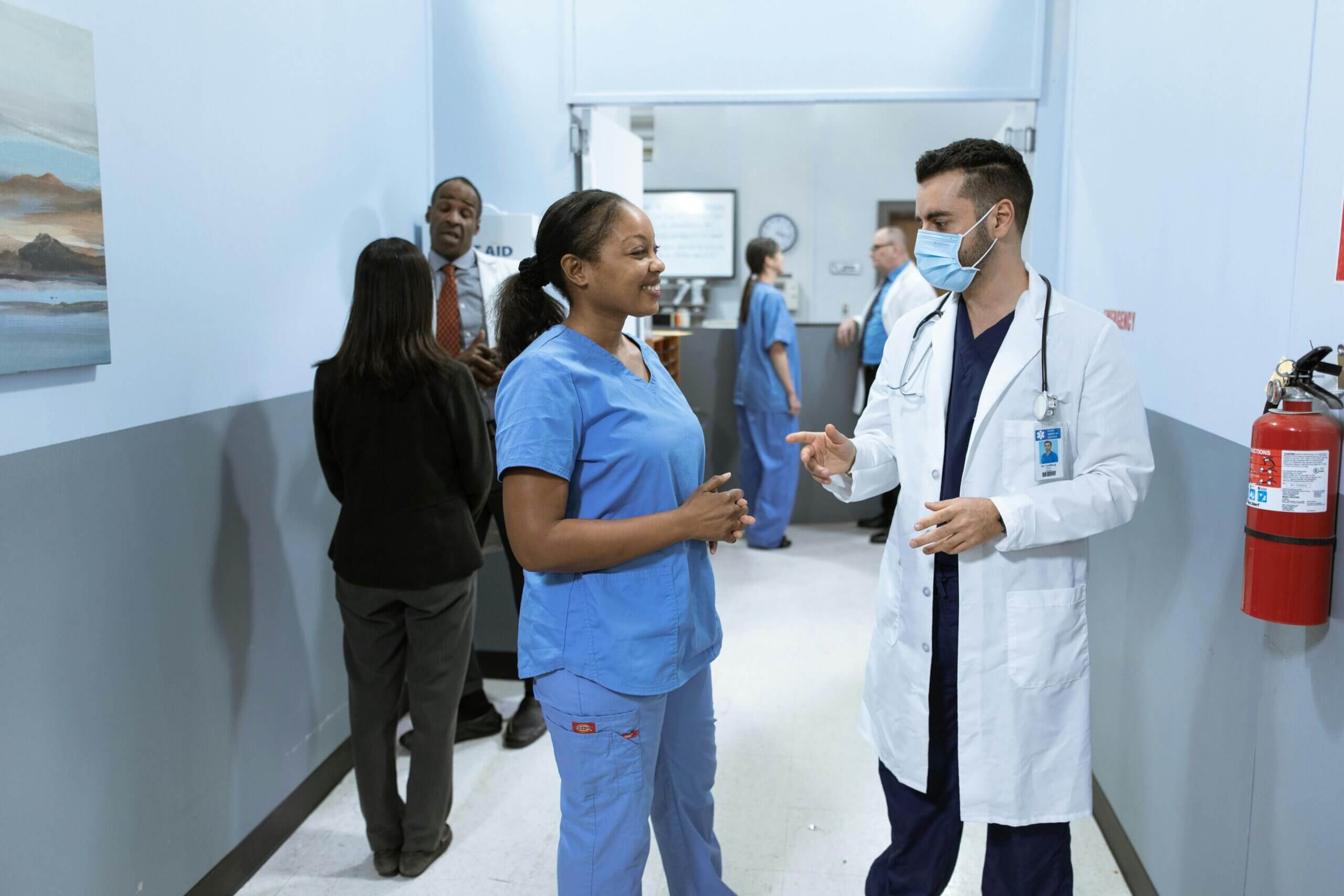 une infimiere souriante en tenue de bloc discute avec un médecin dans un couloir d'hopital
